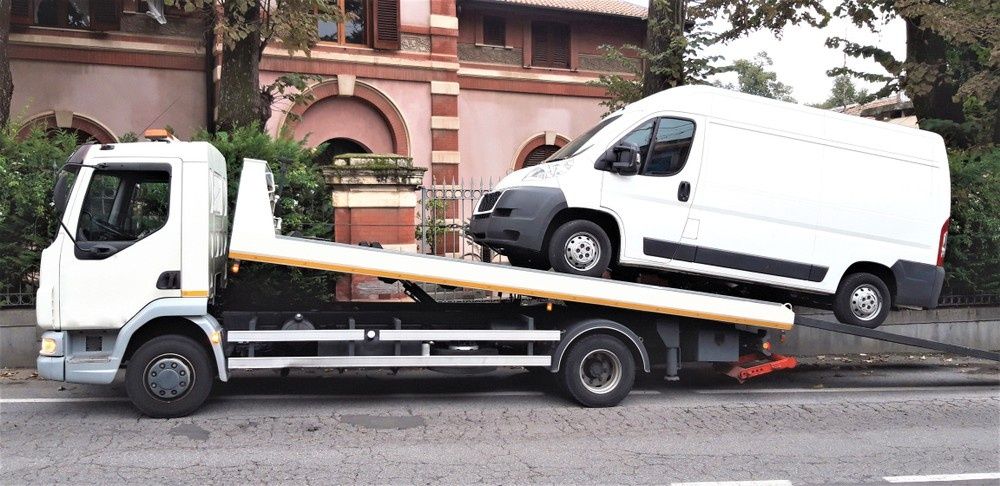A Tow Truck Hauling a White Van on A City Street — A1 Towing in Blue Haven, NSW
