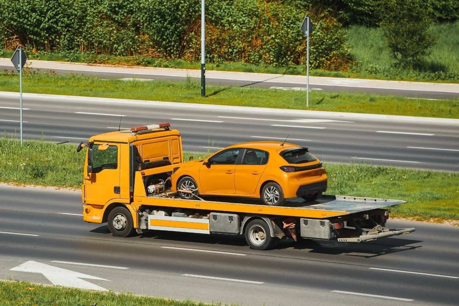 Yellow Tow Truck Carrying an Orange Car on A Highway — A1 Towing in Newcastle, NSW