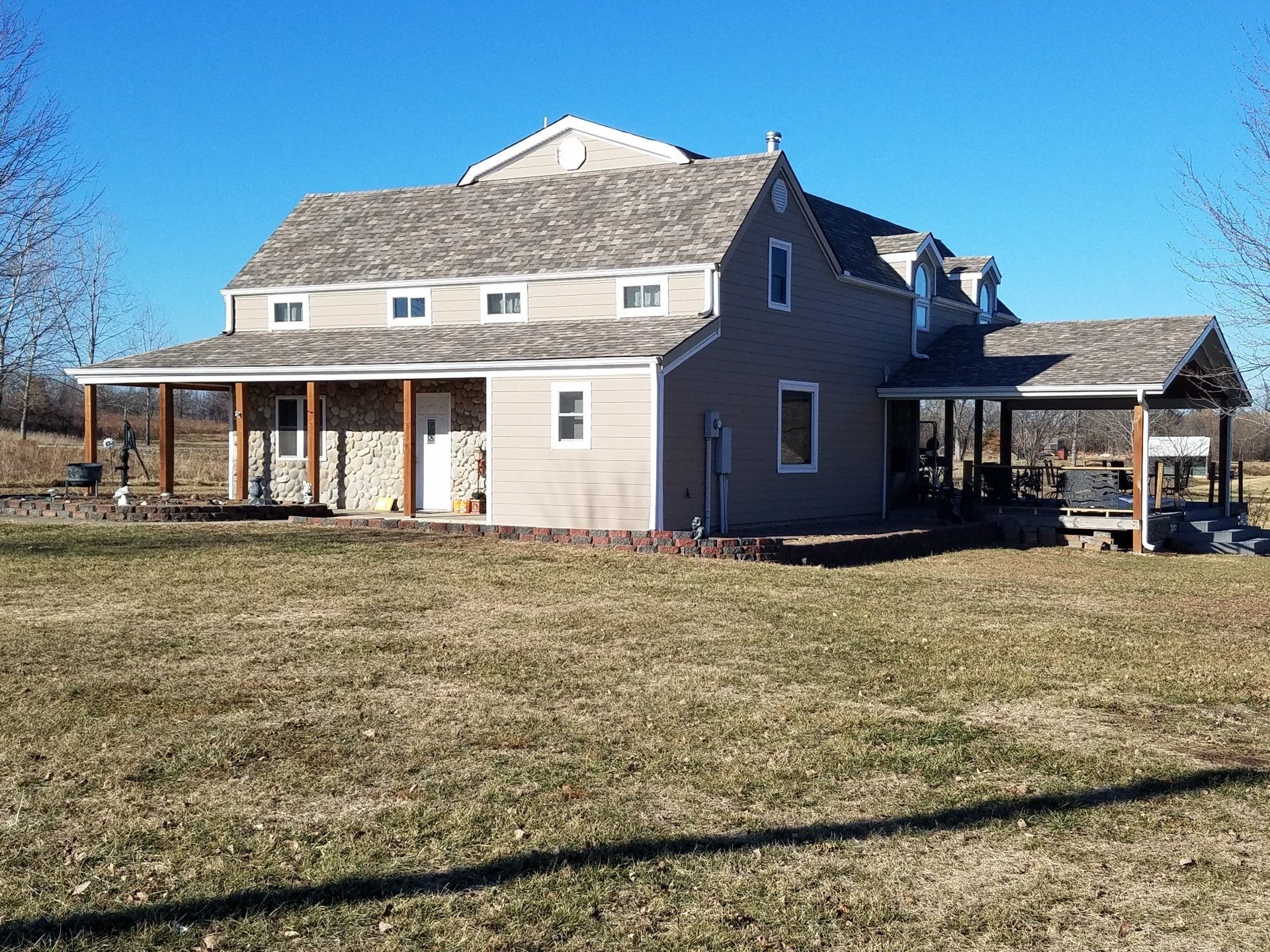 A large house with a porch is sitting in the middle of a grassy field.