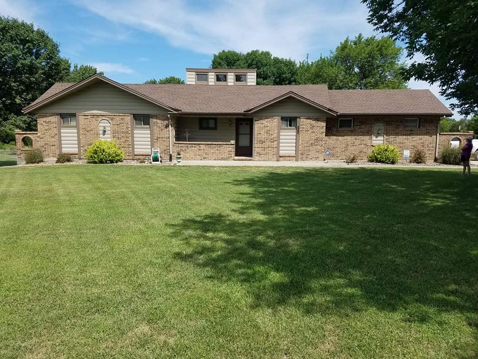 A brick house with a brown roof and a large lawn in front of it