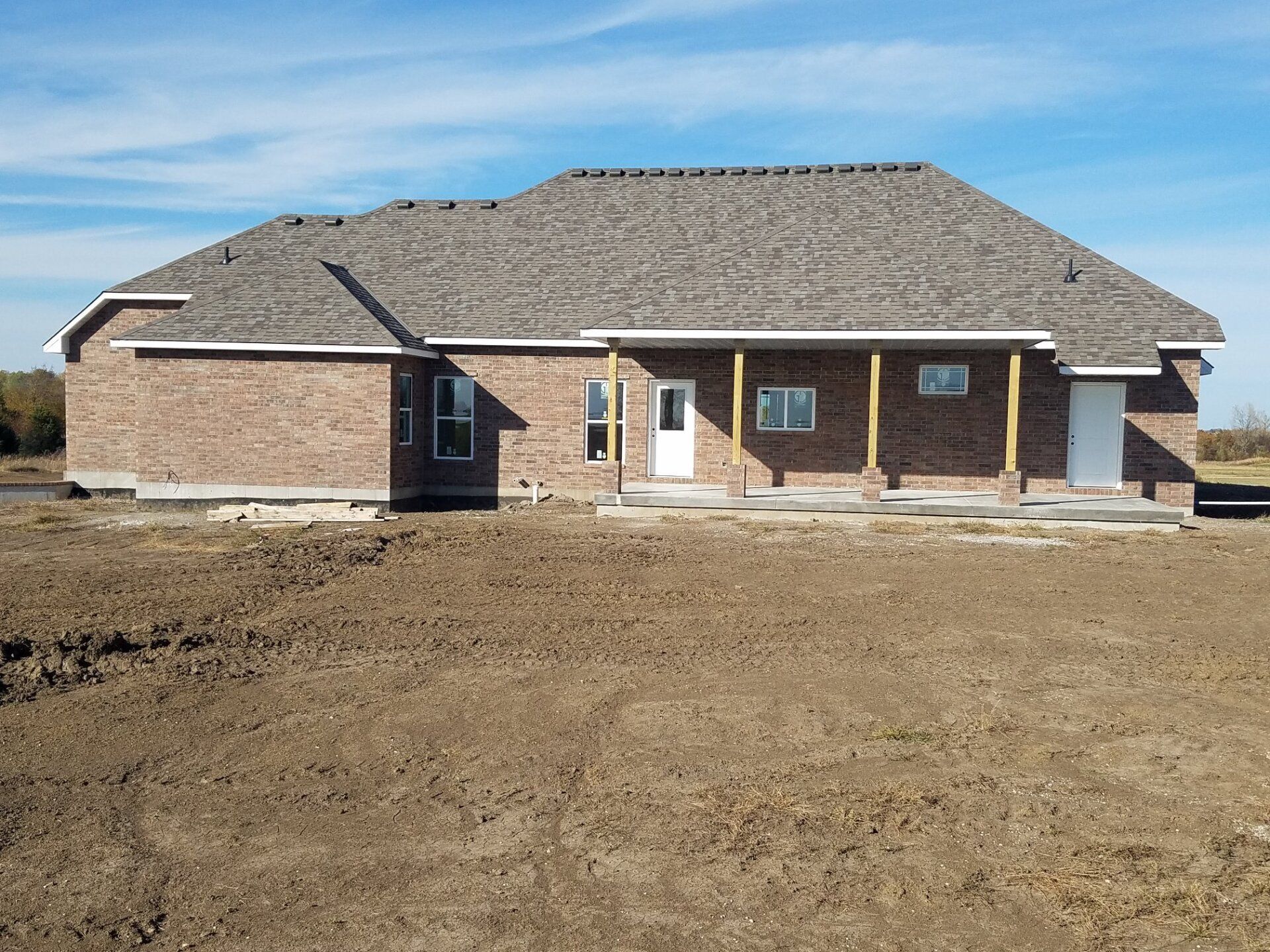 A brick house with a gray roof is in the middle of a dirt field