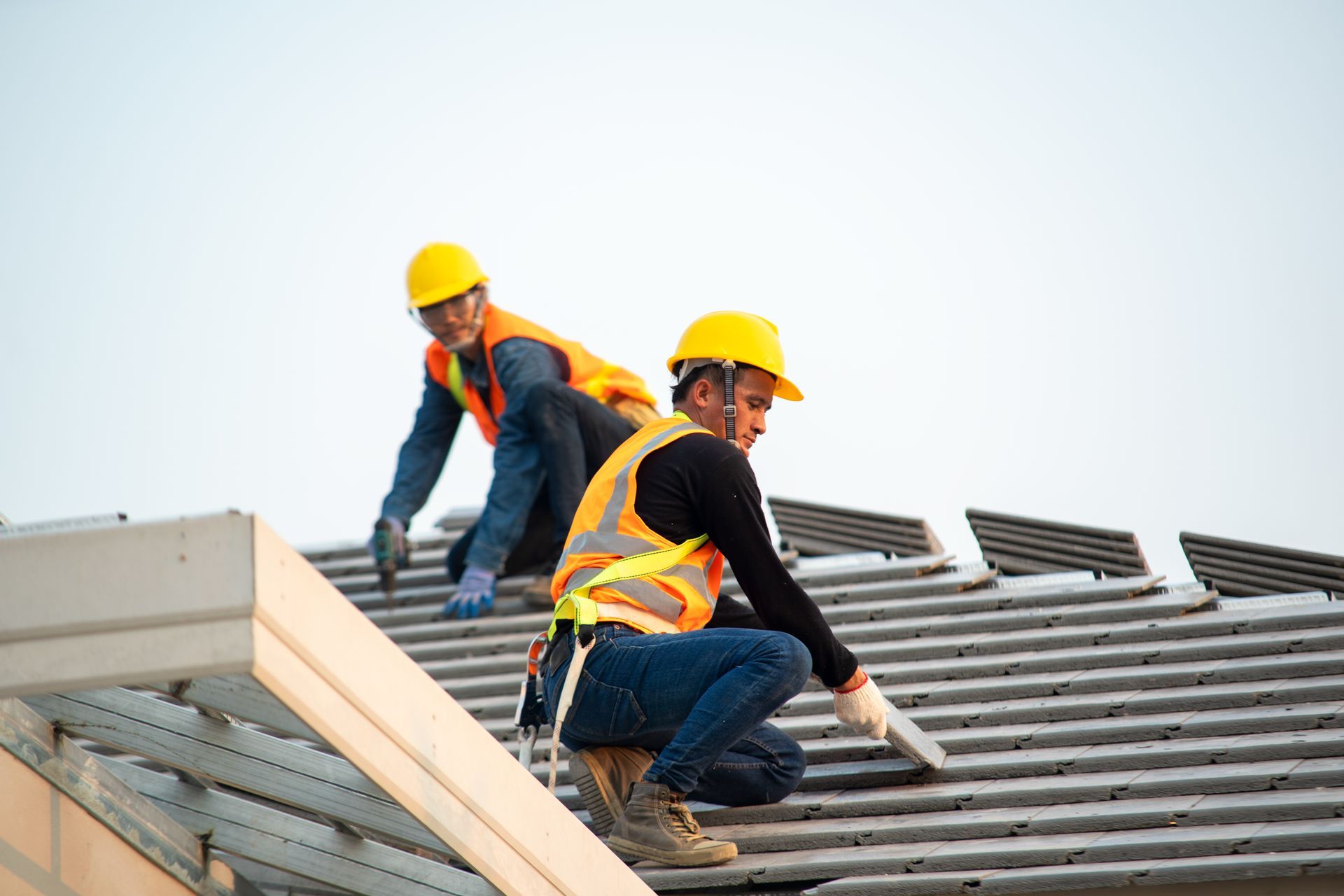 Two construction workers installing metal roofing panels on a building frame, wearing safety gear.
