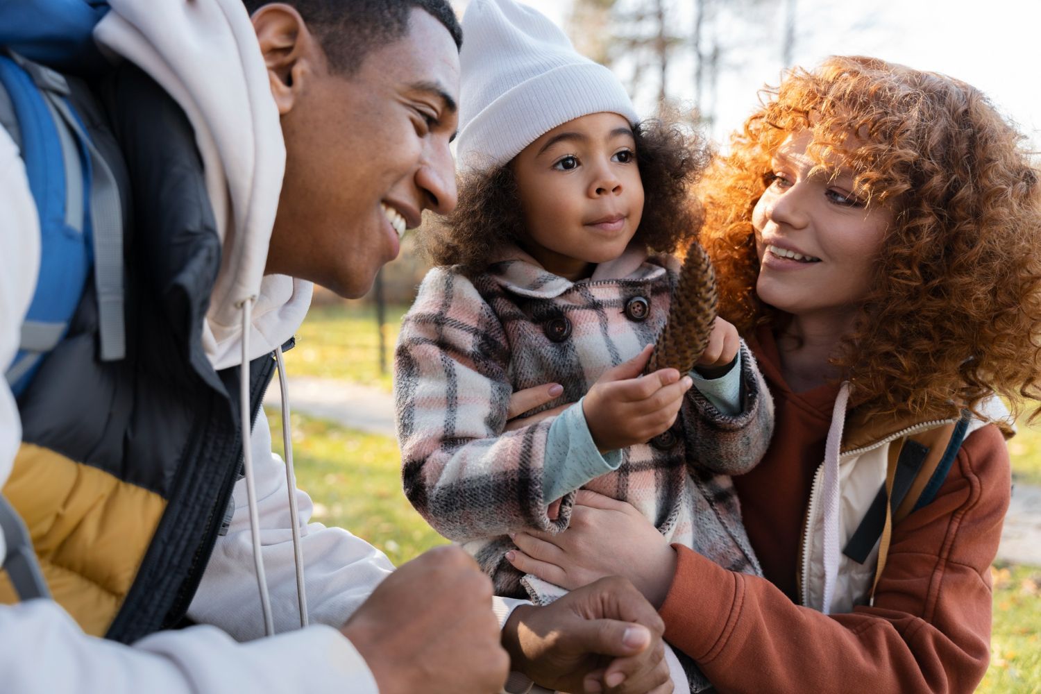 A man and woman are holding a little girl in their arms in a park.