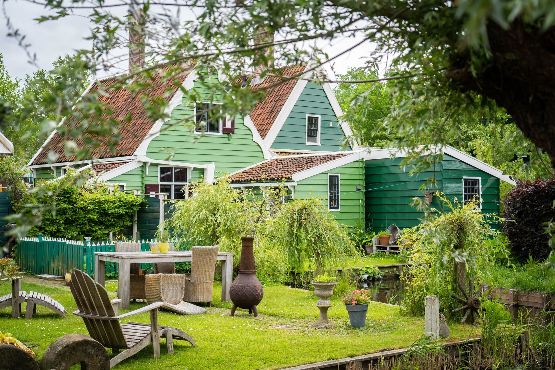 A garden with a table and chairs in front of a green house. 