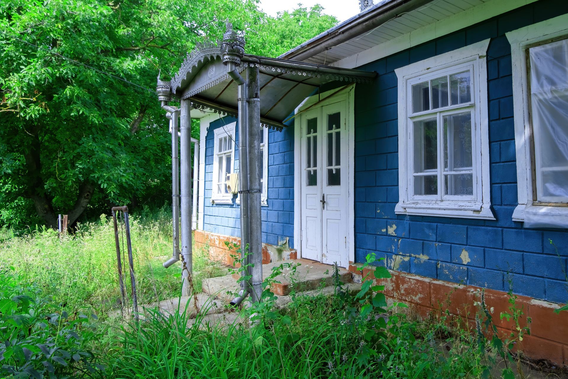 A blue and white house with a porch and trees in the background.