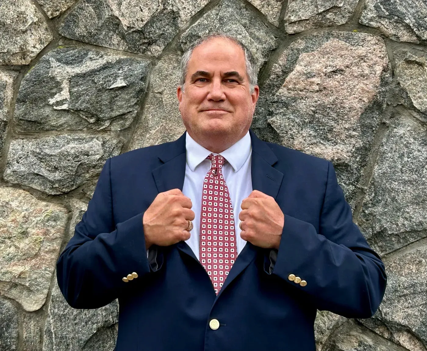 A man in a suit and tie is standing in front of a stone wall.