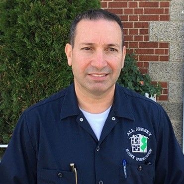 A man in a blue shirt is standing in front of a brick building.