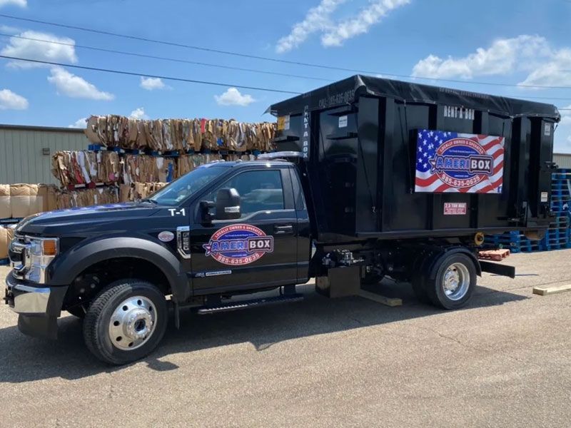 A picture of a black Ameribox truck with a black dumpster on the back in Mandeville, LA.
