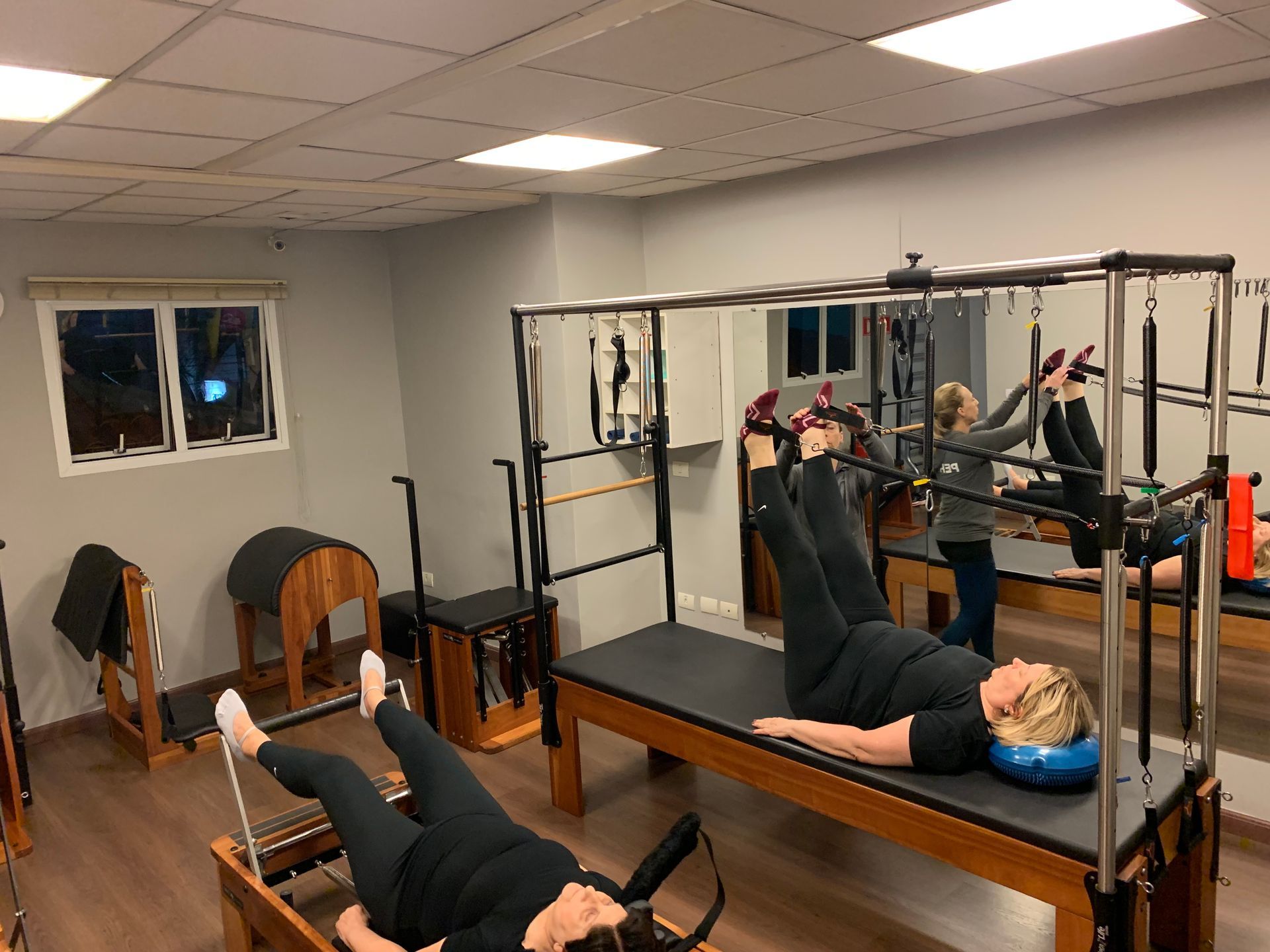Duas mulheres estão deitadas em mesas de pilates em uma academia.