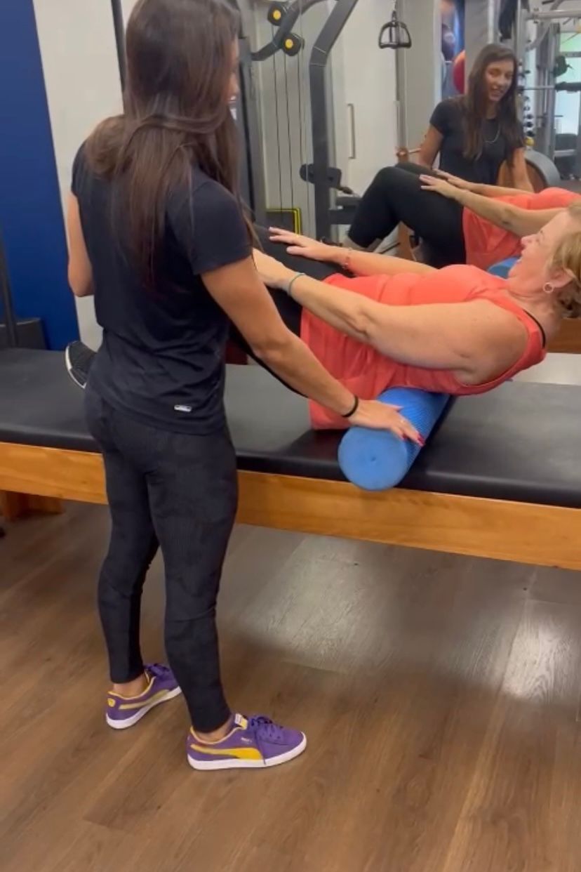 Uma mulher está fazendo exercícios em um tapete de pilates com um rolo de espuma azul.