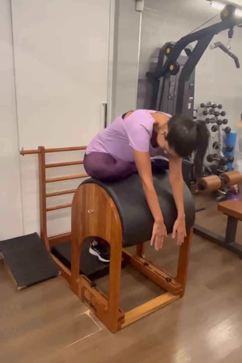 Uma mulher está sentada em uma máquina de pilates em uma academia.
