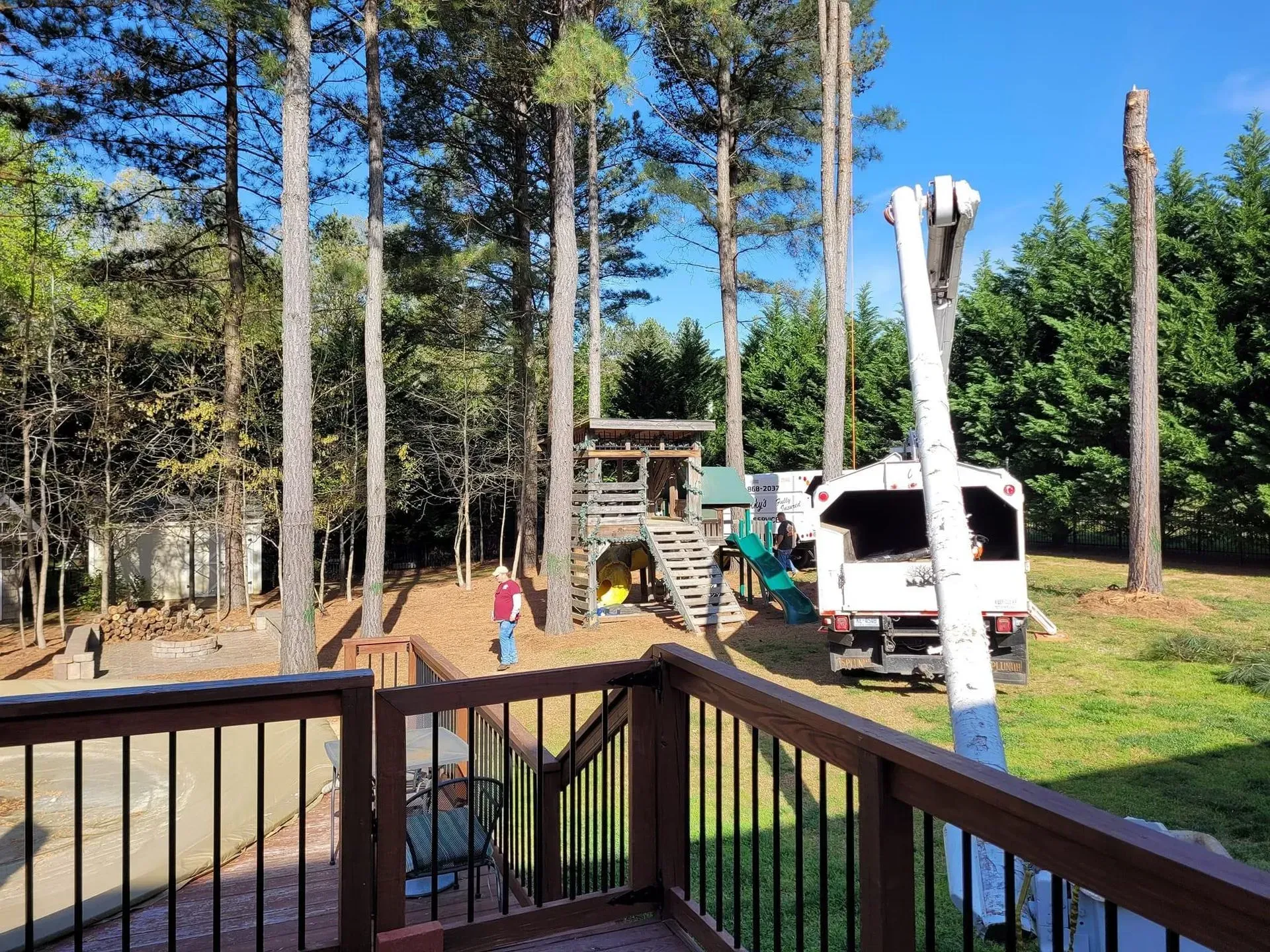 A truck with a lift arm is near a children's playset in a backyard with trees.