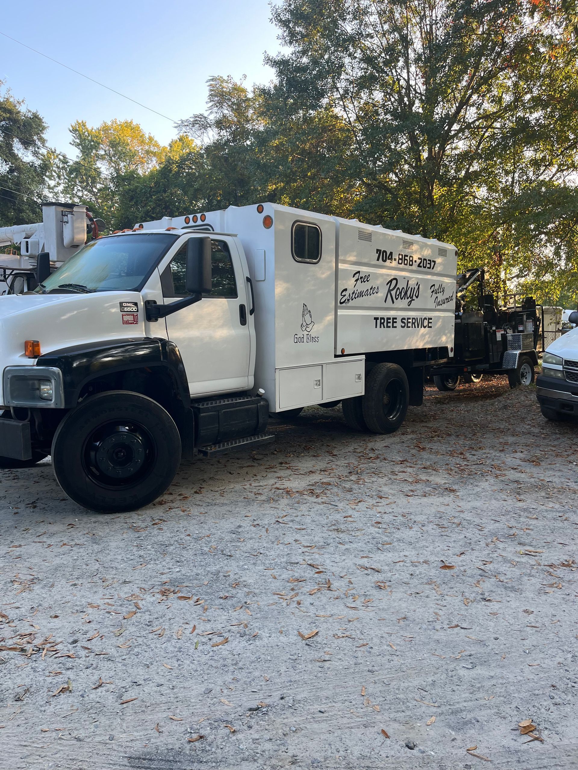 White work truck with black wheels parked on gravel. A trailer is attached.