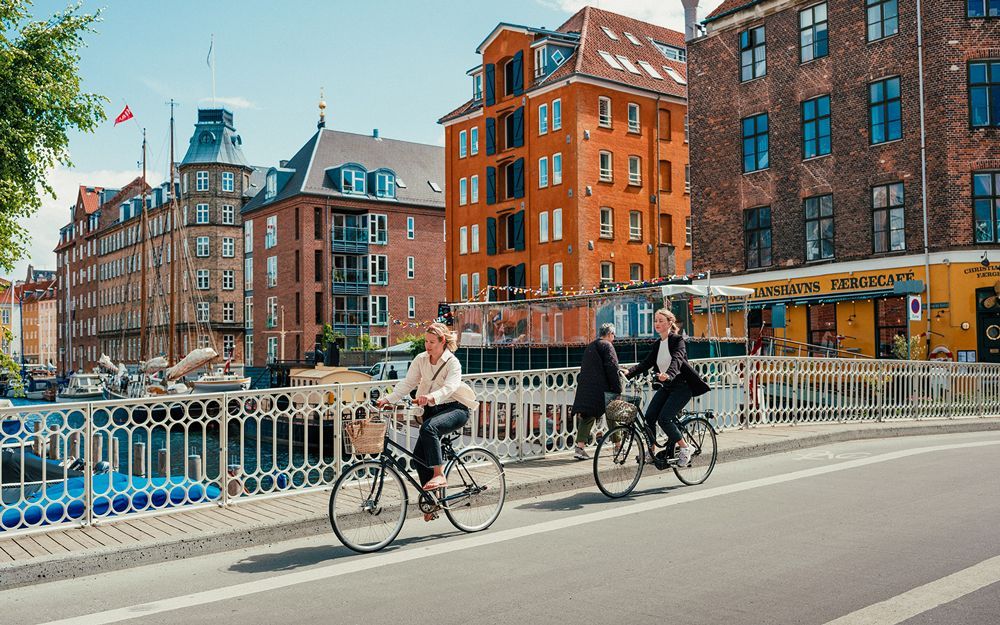 Two people are riding bicycles on a bridge in a city