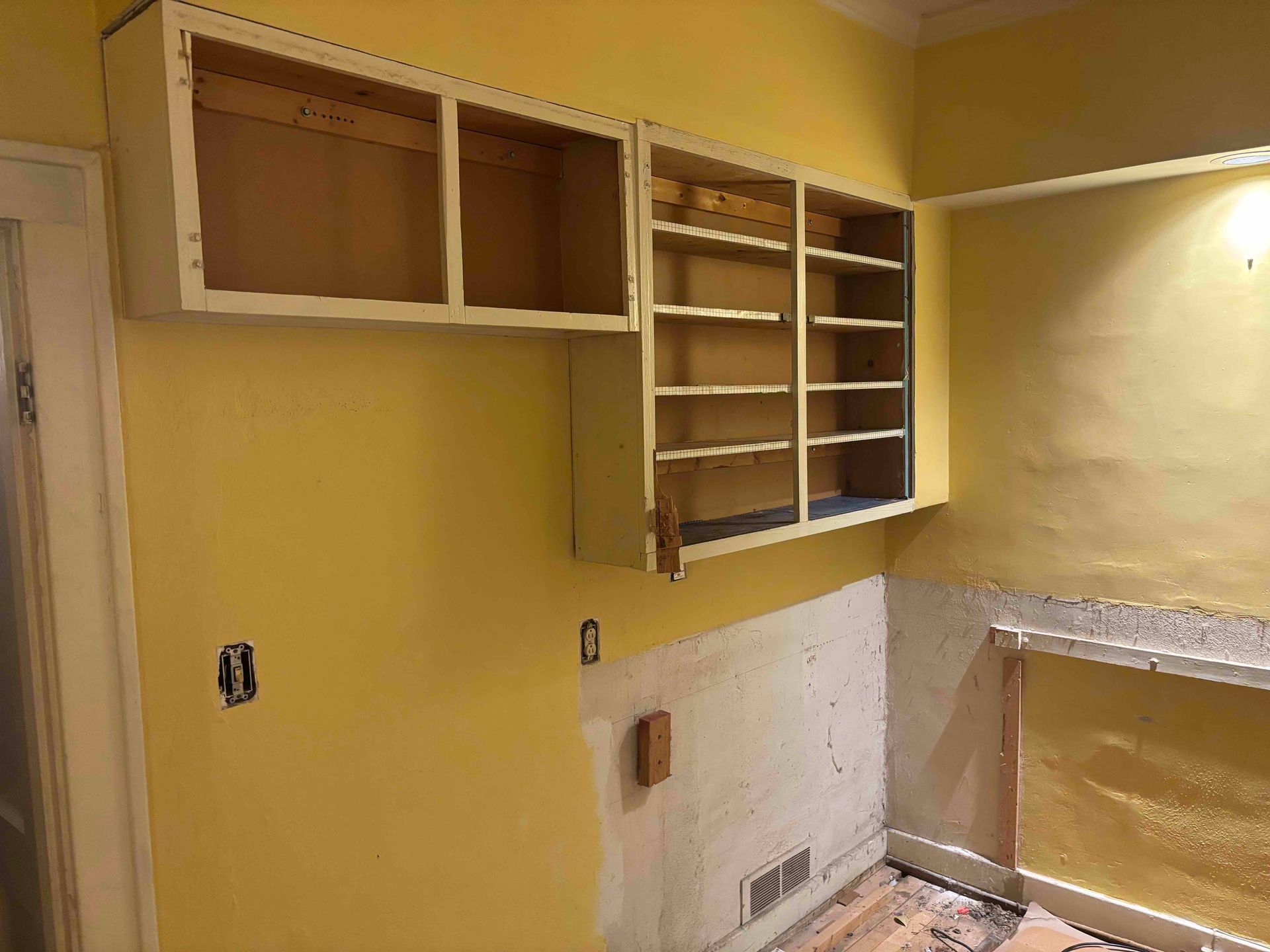 A kitchen under renovation with yellow walls, two exposed wooden cabinet frames, and bare wall sections.