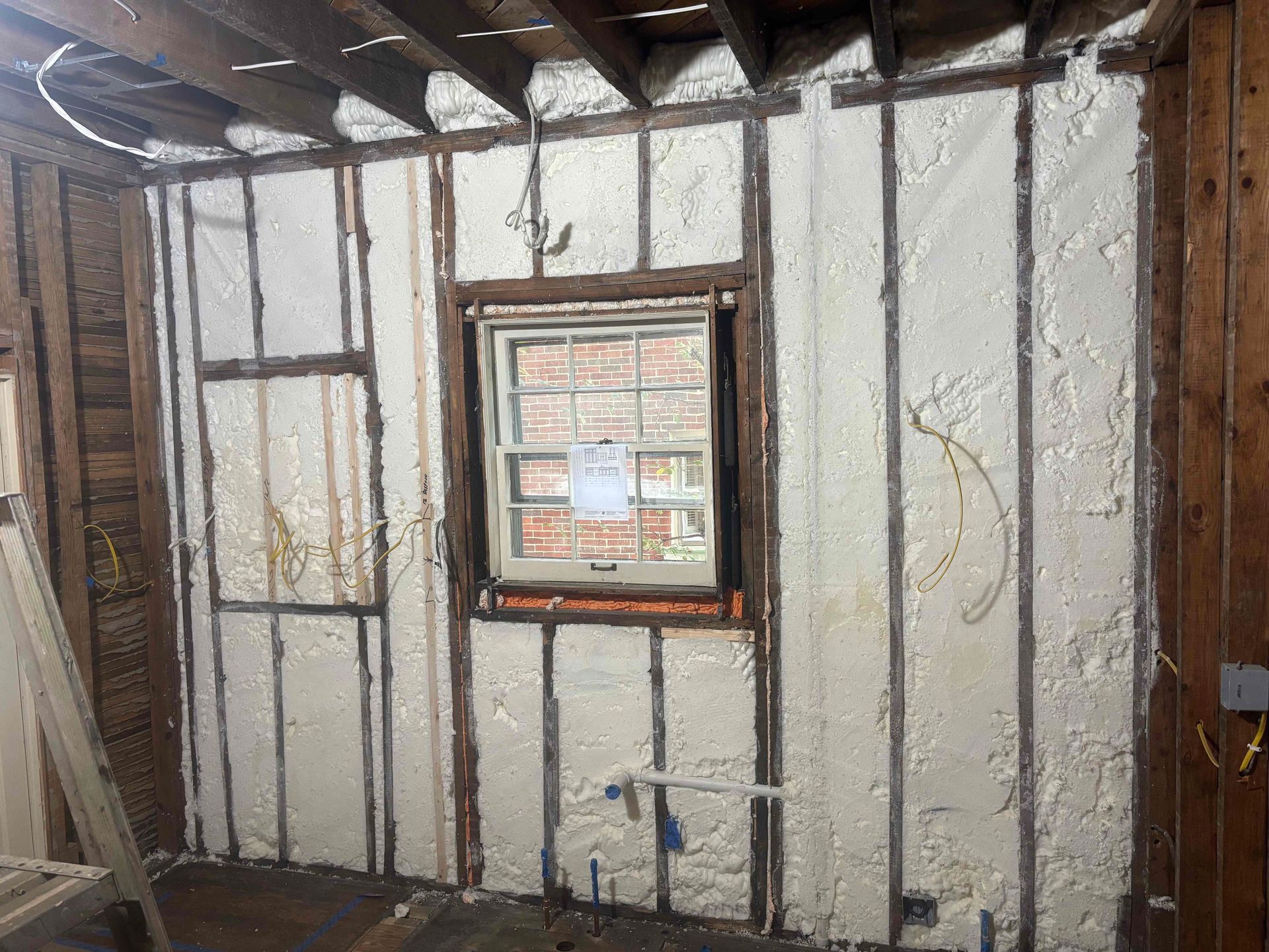 Interior wall studs and a window frame insulated with spray foam in an unfinished room.