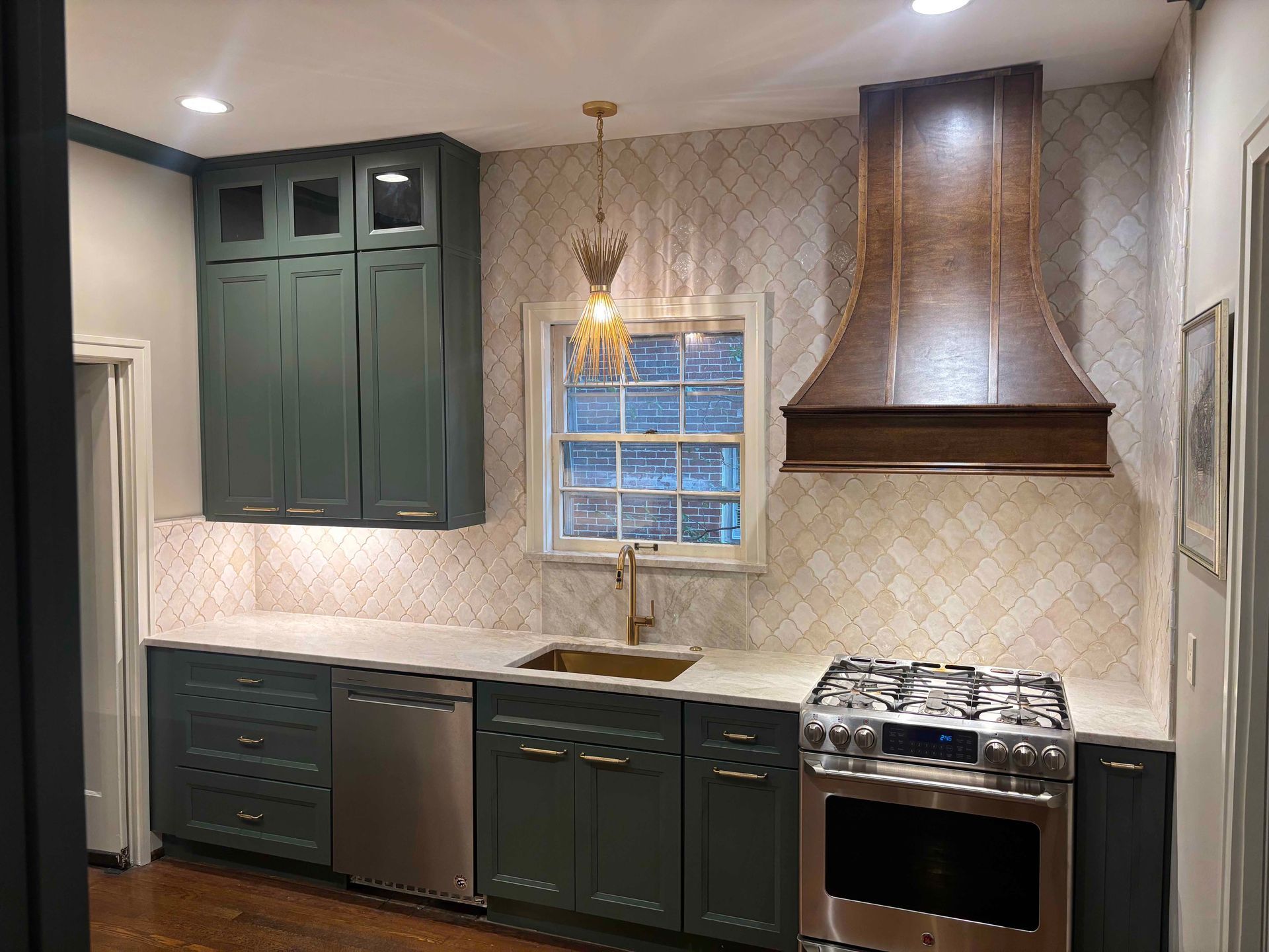A kitchen features deep teal cabinets, a copper vent hood, and a light-tiled backsplash above stainless steel appliances.