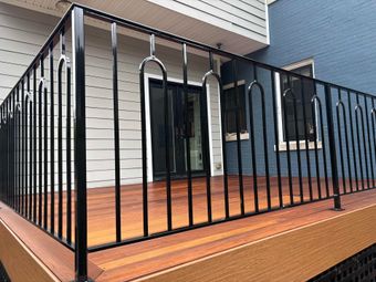 Black metal railing on a wooden deck in front of a house, with a door and windows visible.