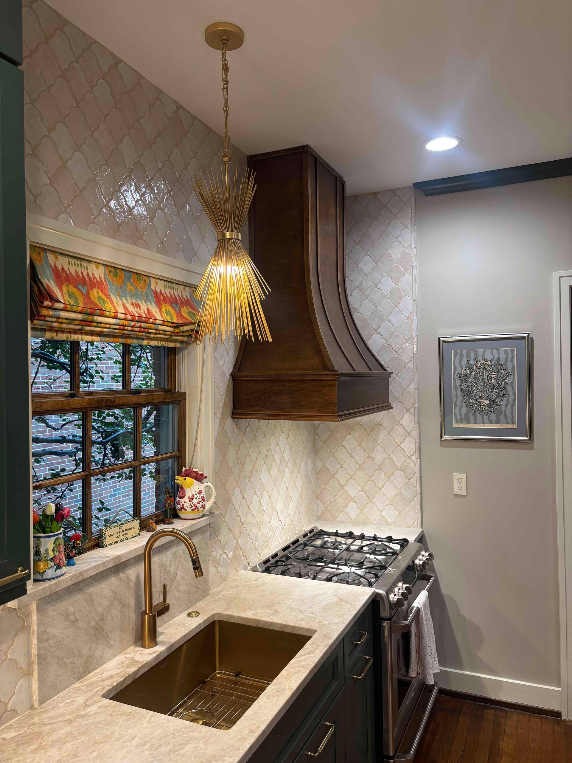 A kitchen with dark green cabinets, white patterned backsplash, a stainless steel stove, and a wooden range hood.
