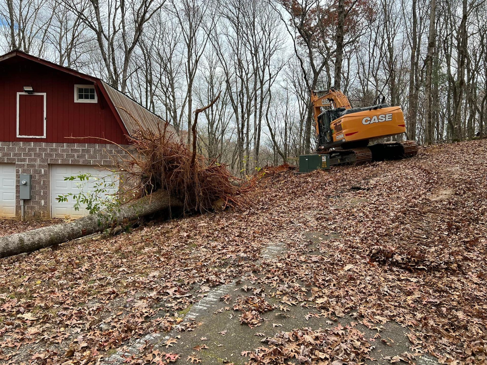 A large excavator is sitting on top of a pile of leaves in front of a barn.