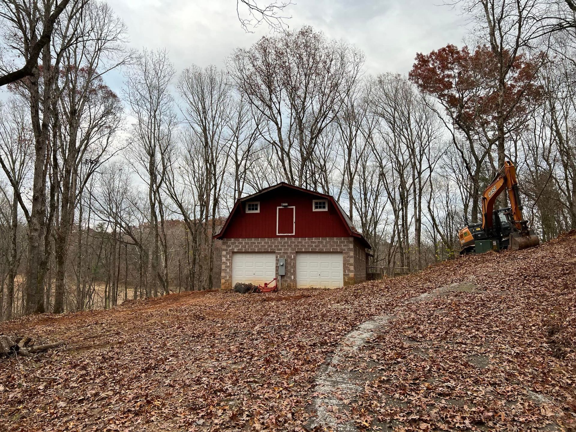 A red barn is surrounded by trees and leaves in the middle of a forest.
