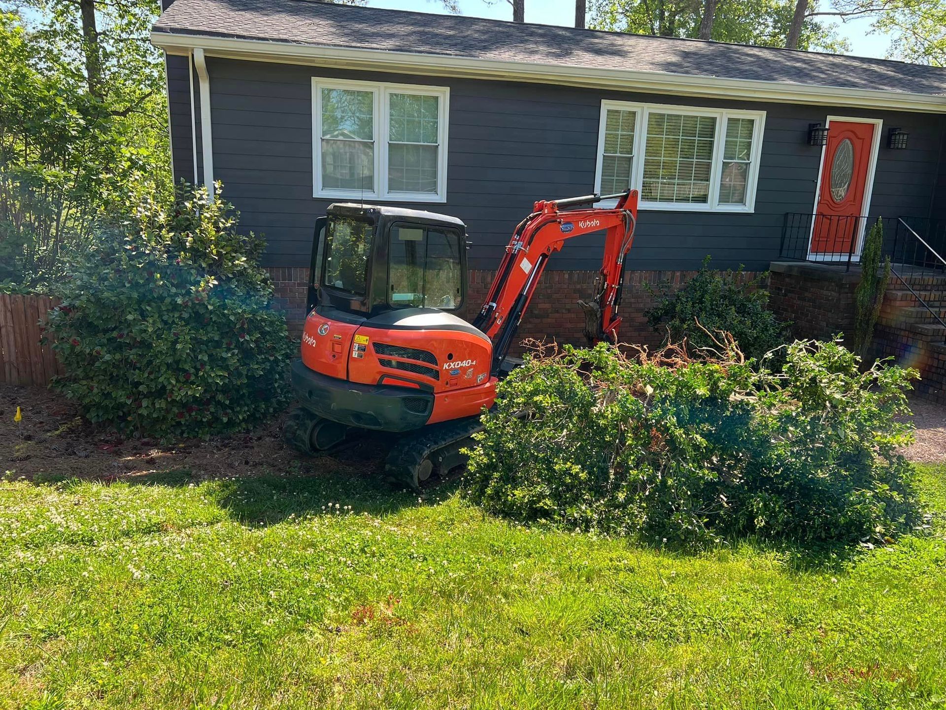 A small orange excavator is parked in front of a house.