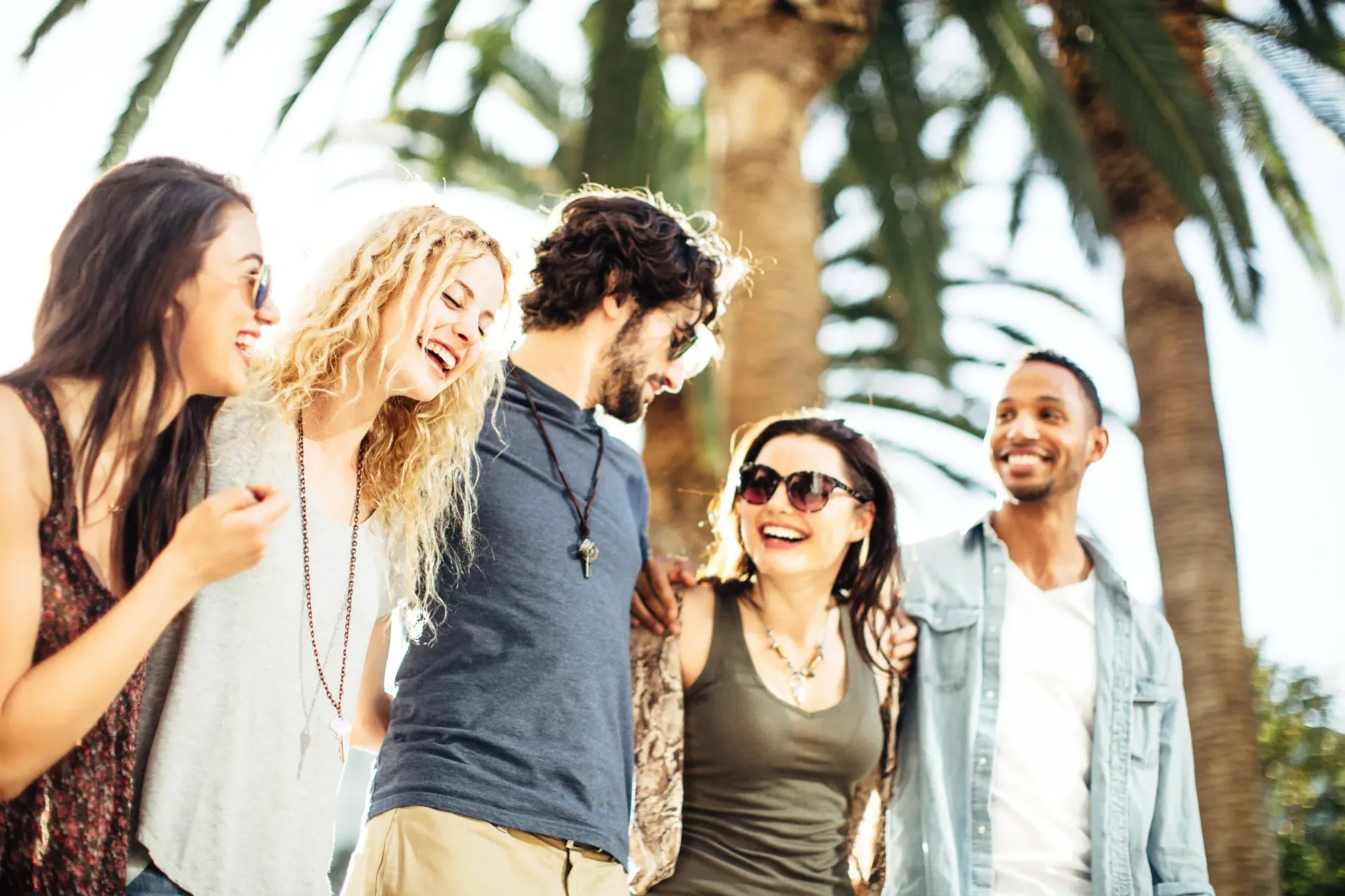 Group of friends laughing together under a palm tree.