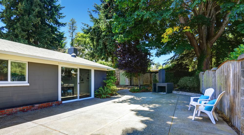 Backyard With a Gray House, Concrete Patio, Trees, Wooden Fence — Atherton Tableland Concreting in Yungaburra, QLD