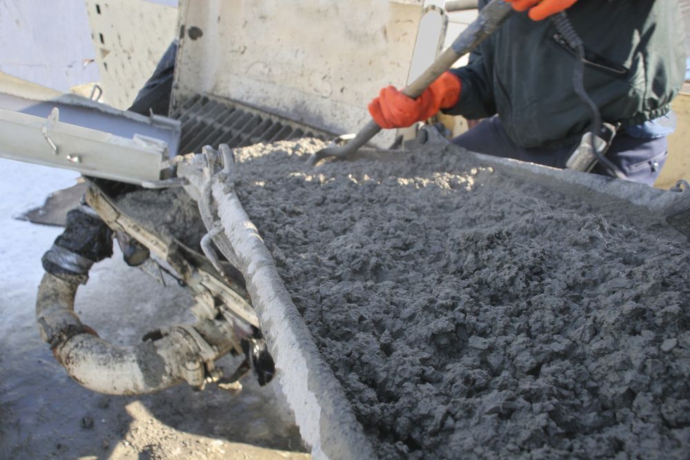 Person in Orange Gloves Shoveling Wet Concrete From a Chute — Atherton Tableland Concreting in Dimbulah, QLD