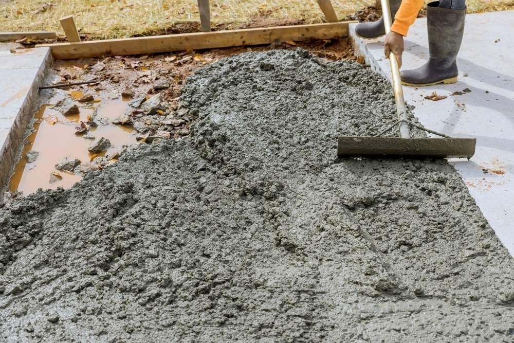 A Man is Spreading Concrete on a Sidewalk With a Rake — Atherton Tableland Concreting Pty Ltd in Mareeba, QLD