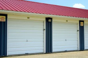 Storage units with white doors, dark blue trim, and red roof under a blue sky.