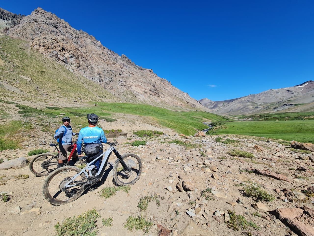 Dos personas van en bicicleta por un camino de tierra en las montañas.