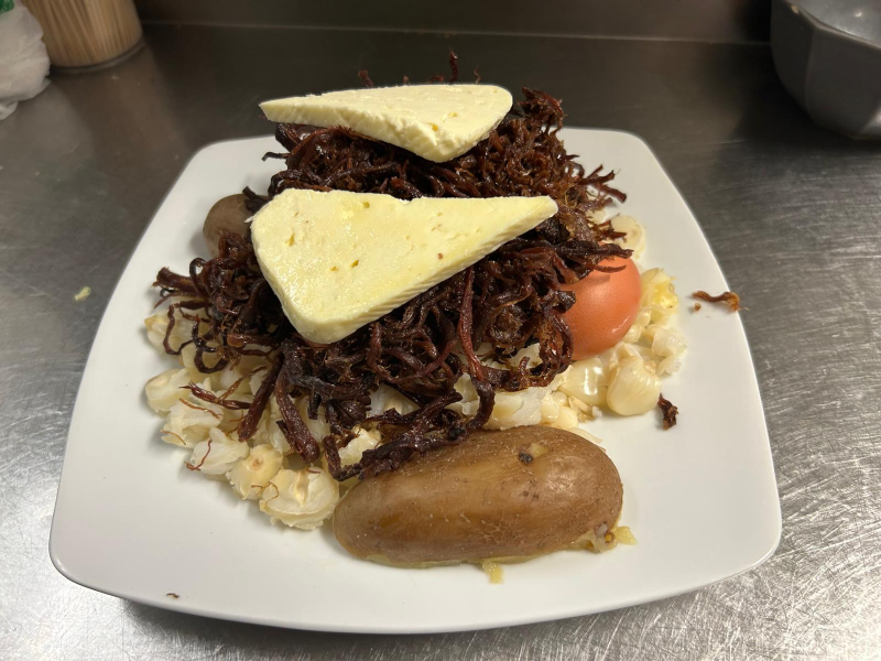 Piatto di cucina peruviana: patate lesse, chicchi di mais, cipolle fritte, pomodoro e formaggio.