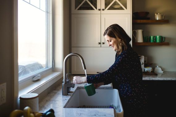 A woman is washing dishes in a kitchen sink.