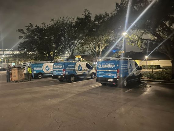 A row of blue and white vans are parked in a parking lot at night.