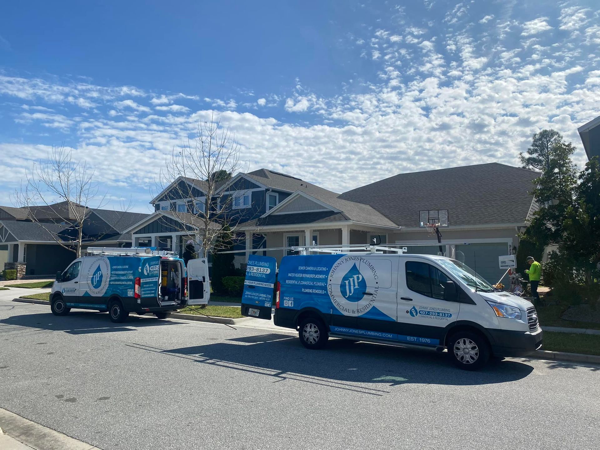 Johnny Jones Plumbing - Two vans are parked on the side of the road in front of a house.