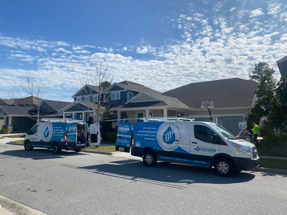 Two vans are parked on the side of the road in front of a house.