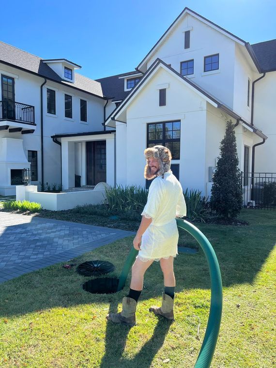 A man is standing in front of a white house with a green hose.