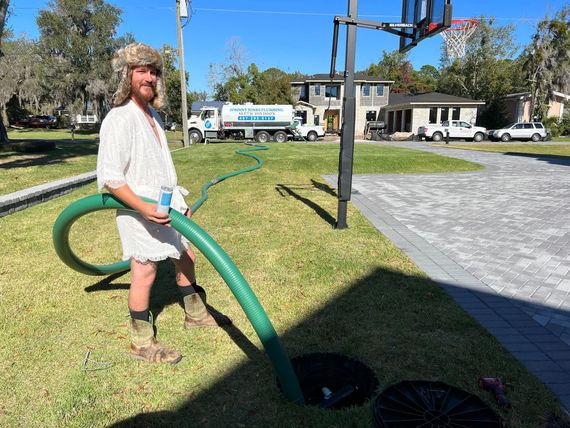 A man is standing in the grass holding a green hose.