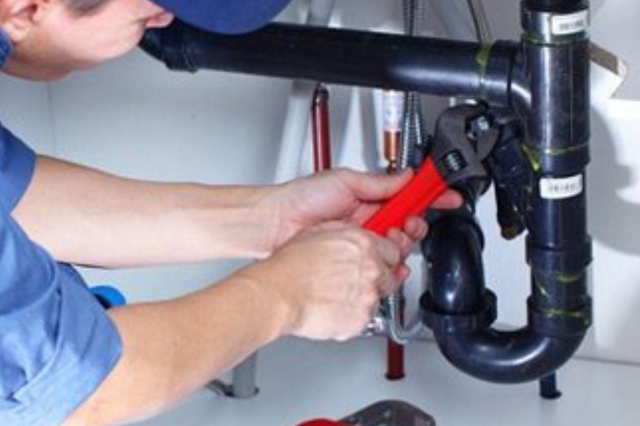 A man is fixing a pipe with a wrench.