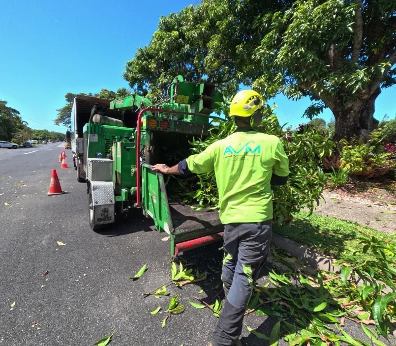 A Man in A Green Shirt Is Standing Next to A Tree Chipper — Advanced Vegetation Management in Edge Hill, QLD