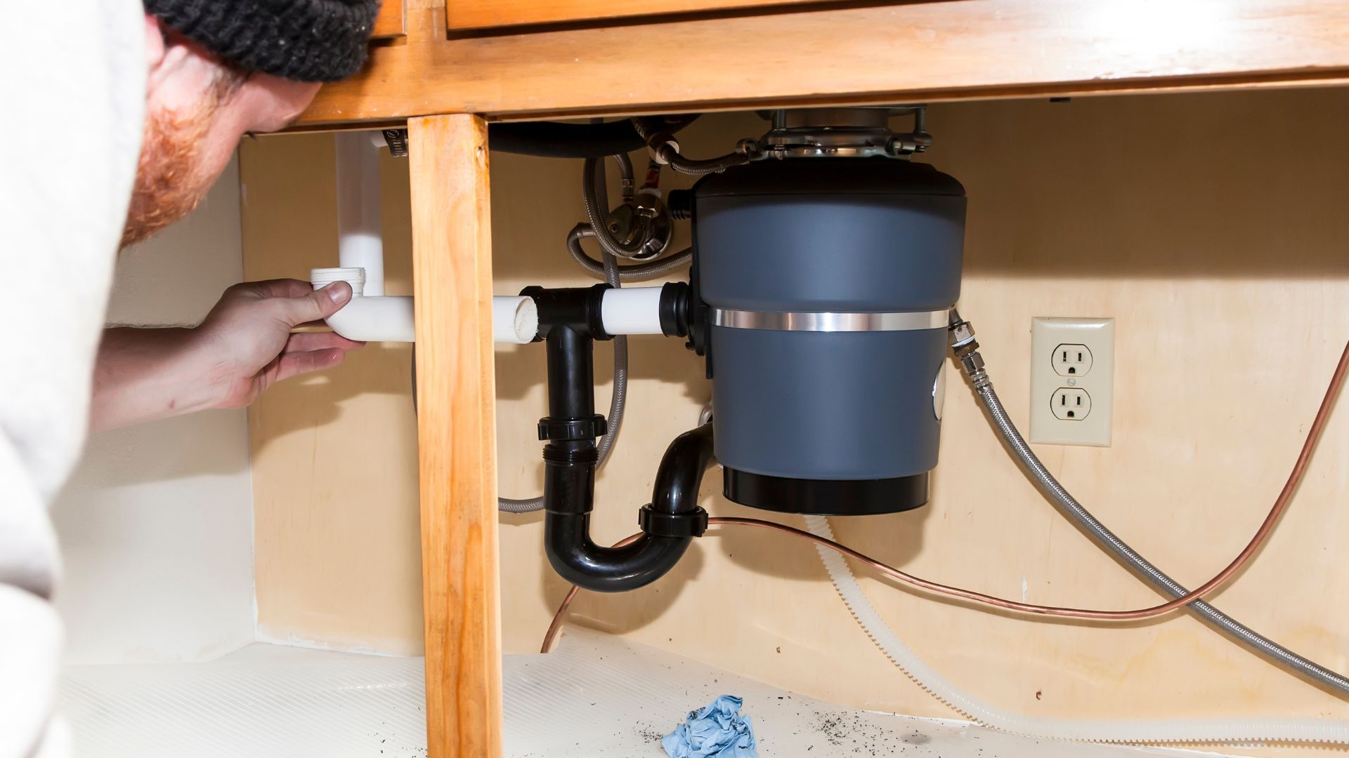 A man is fixing a garbage disposal under a kitchen sink.