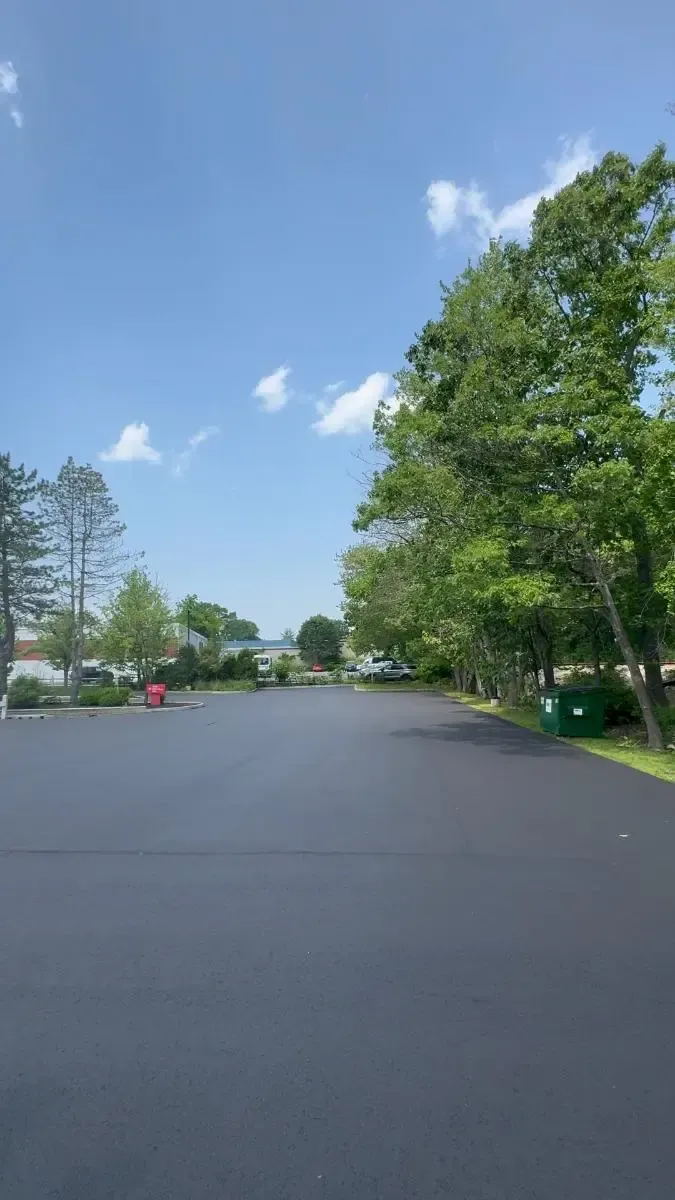 Black asphalt parking lot, trees on the right, light blue sky with wispy clouds.
