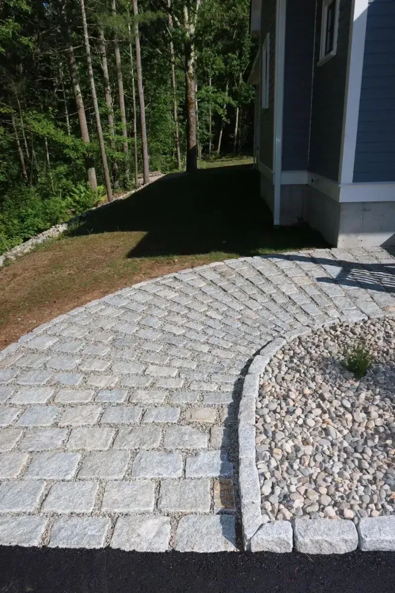 Curved gray stone walkway leading to a blue house, bordered by small stones.