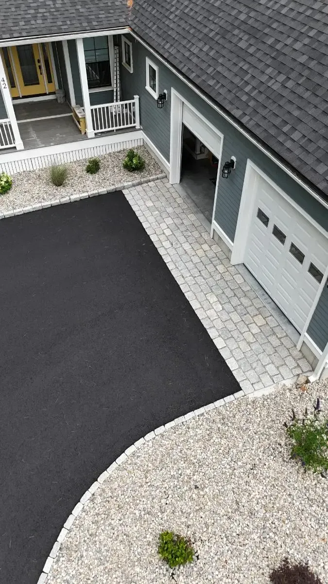 Driveway with black asphalt and stone edging, leading to garage with a white door and blue siding.