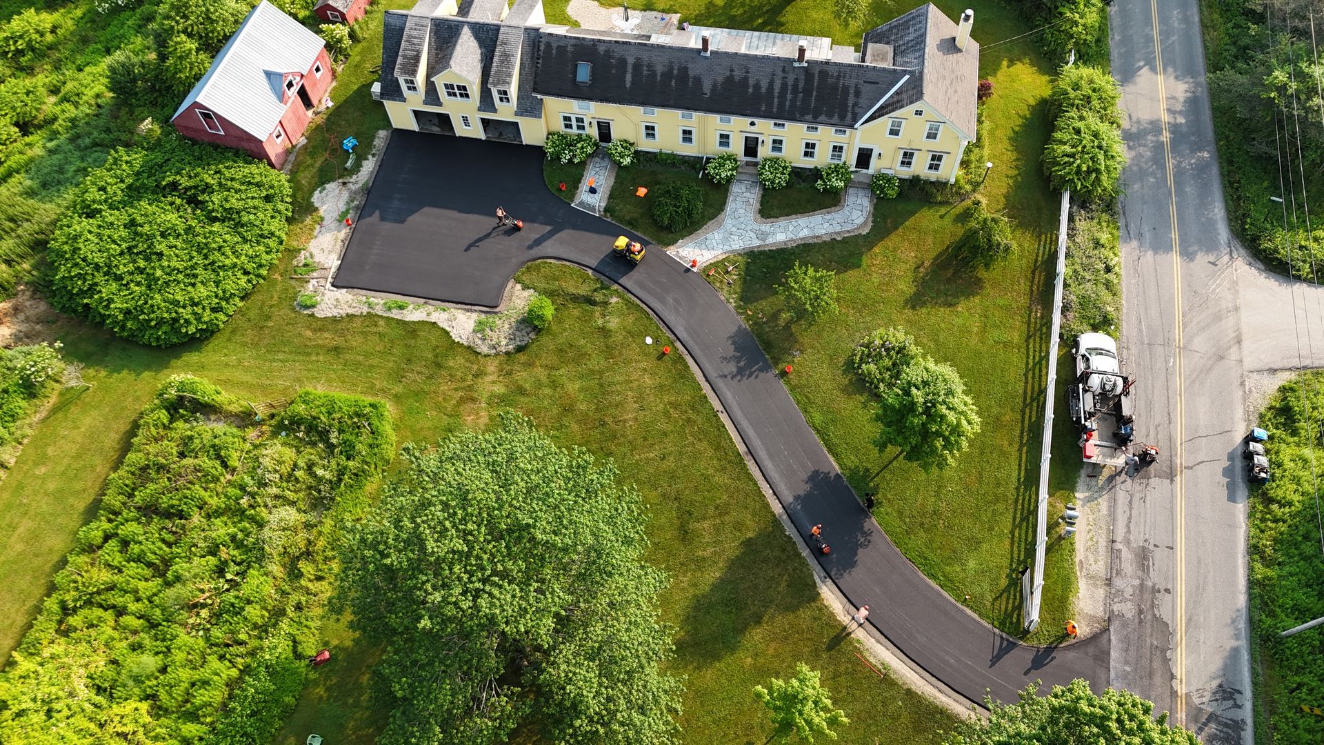 House with teal siding, dark driveway, and green lawn under a blue sky, framed by trees.