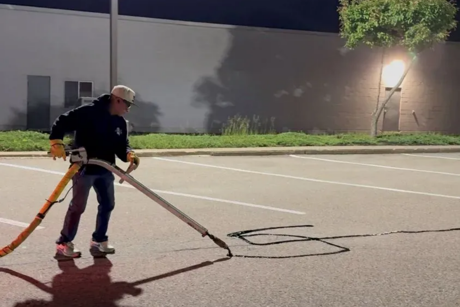 Person using a machine to apply dark sealant to a parking lot at night.