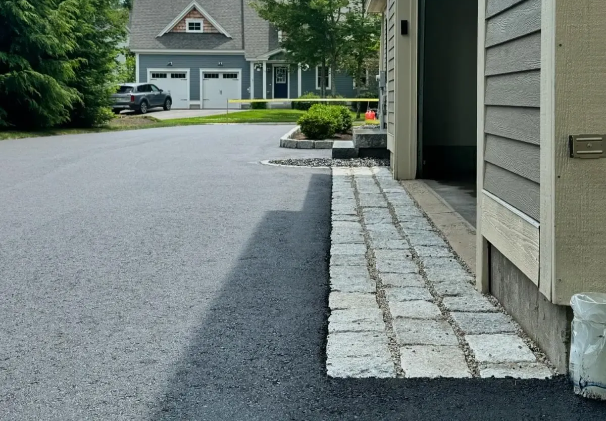 Stone paved walkway curving to a paved driveway, with trees in background.
