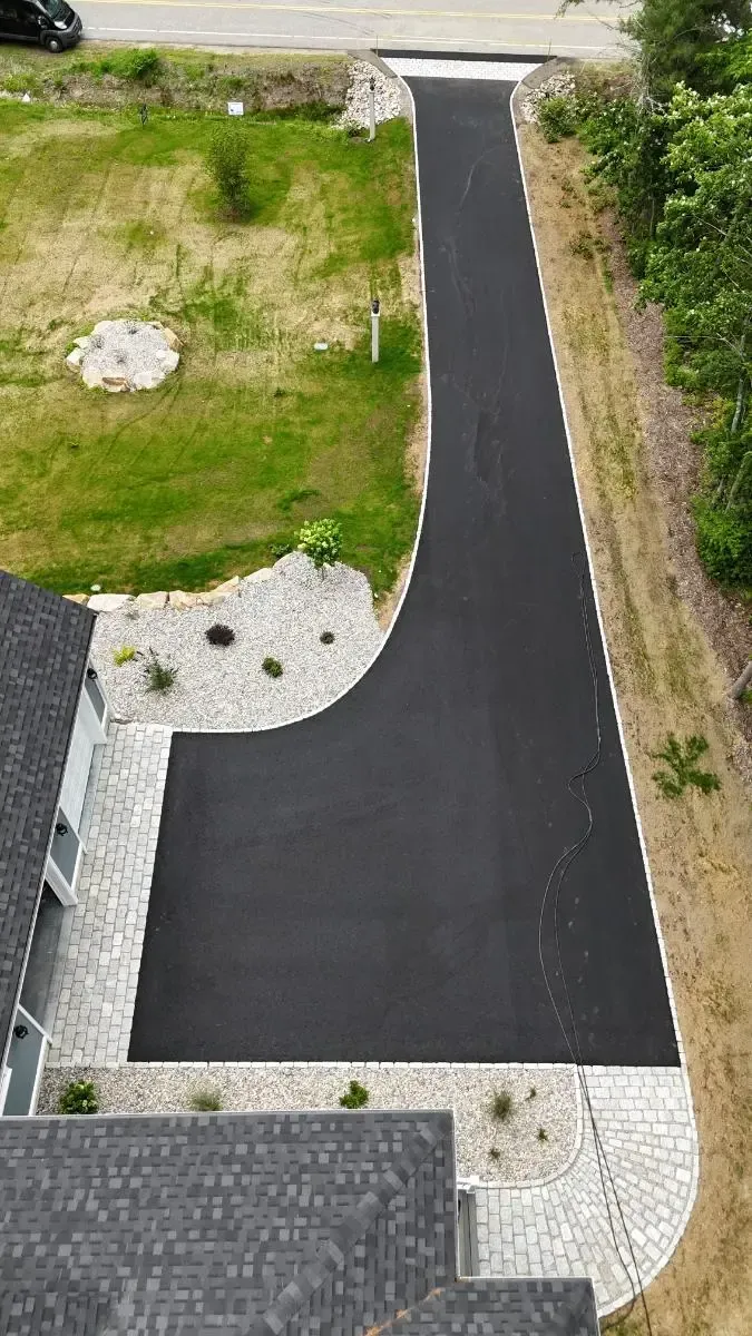 Asphalt driveway curving from street to house with gravel and landscaping around edges.