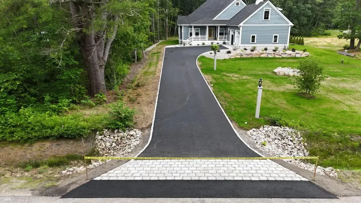 Green garage doors with arched windows; blue siding, a stone border and asphalt driveway.